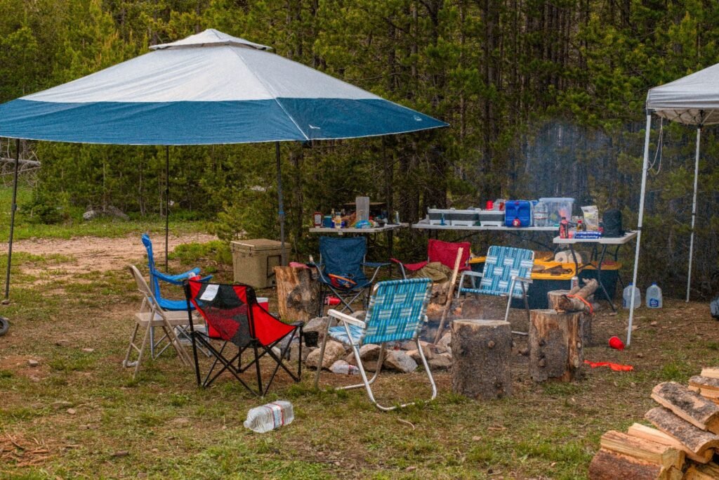 Camping Setup Order: What to Set Up First (And Why It Matters) Cluttered family campsite with canopy tents, camp chairs, fire ring, and cooking tables in forest clearing.