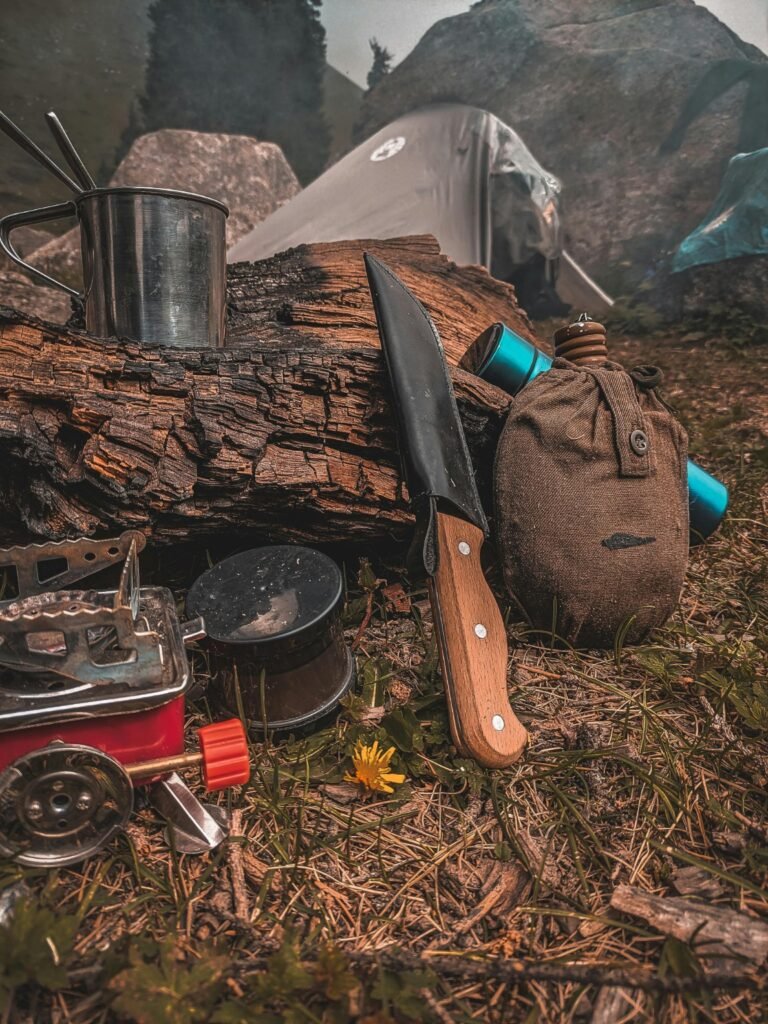 What to Pack for Your First Camping Trip (Beginner Camping Checklist) Essential camping gear for a first camping trip including stove, knife, mug, and tent at a campsite